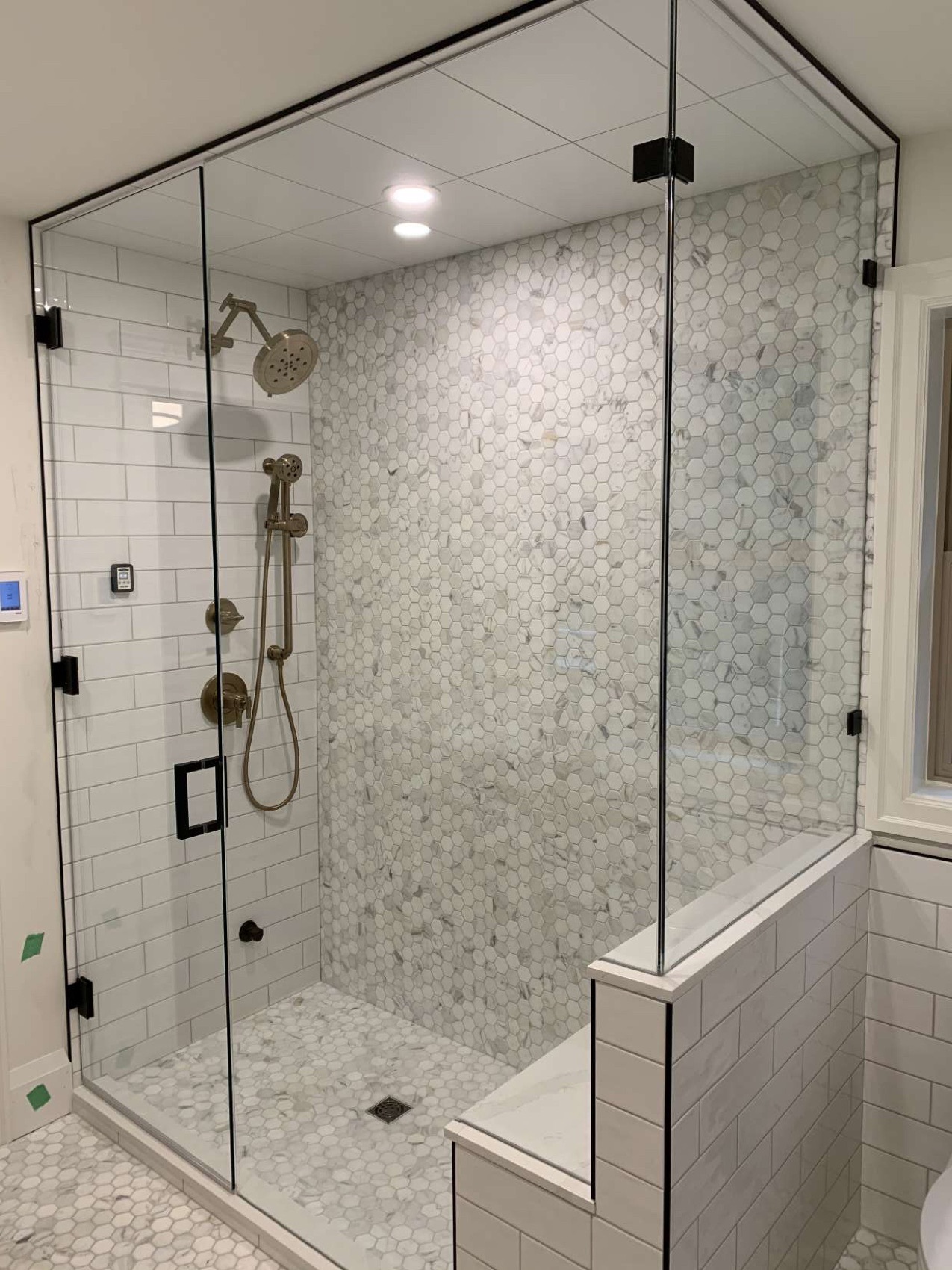 Frameless glass walk-in shower with Carrara marble hexagon mosaic, white subway tile and brushed-brass fixtures, installed by Yurtec Interiors